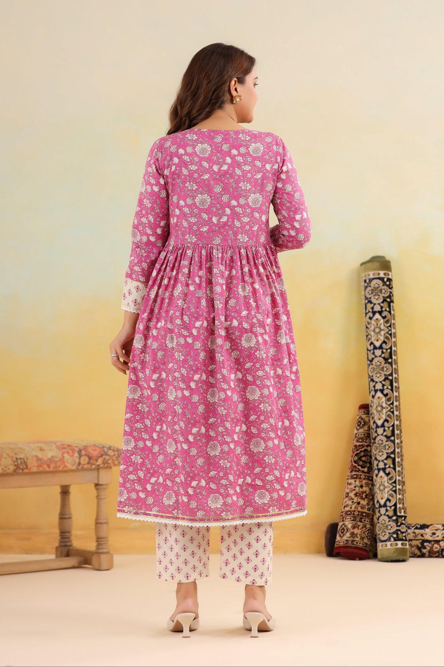 Woman wearing a pink floral dress with a yellow gradient wall and traditional instruments.