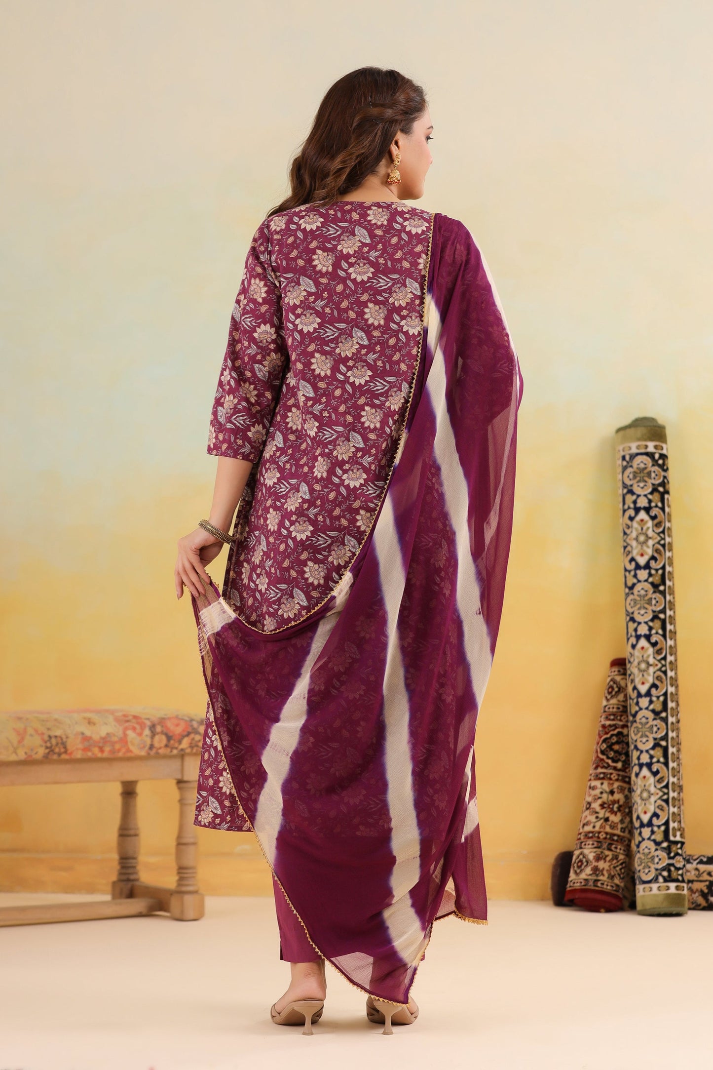 Woman wearing a purple saree with a floral pattern against a gradient wall.