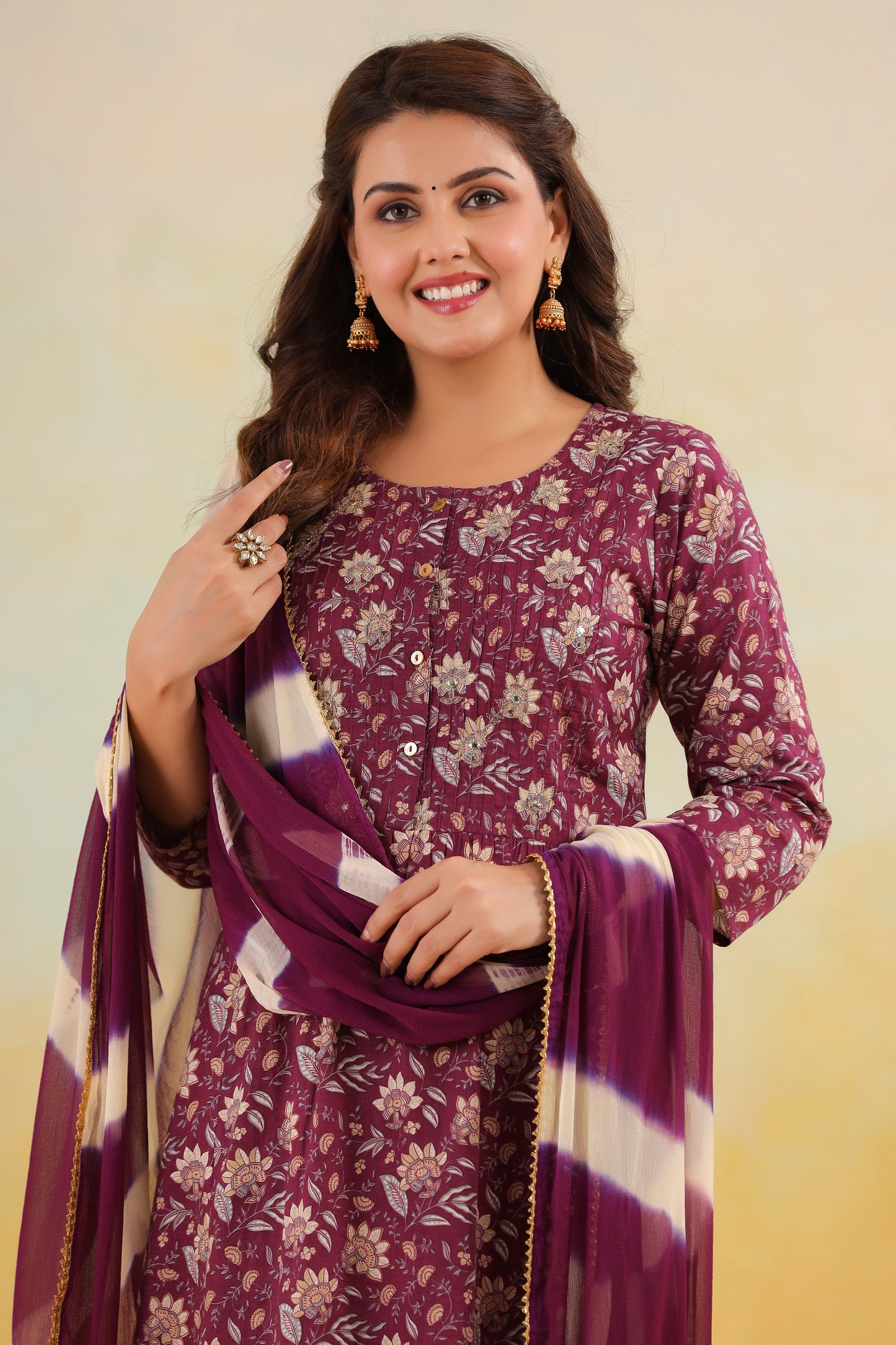 Woman wearing a purple floral outfit with a matching dupatta on a beige background