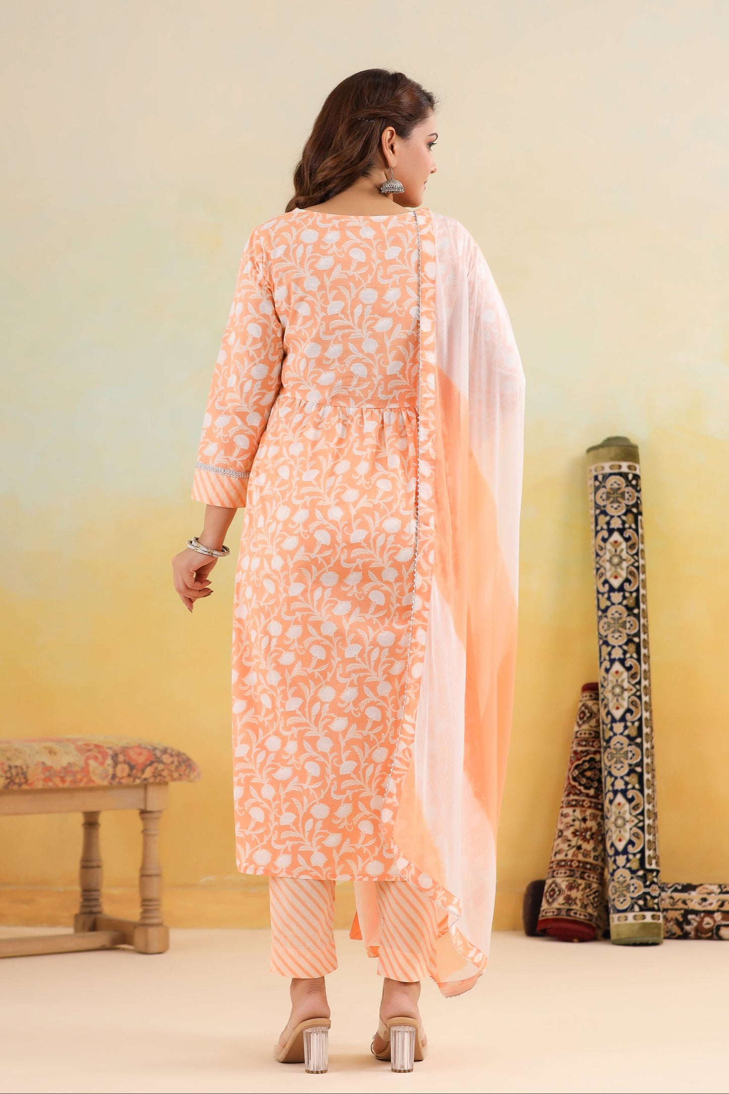Woman wearing a peach-colored kurta with a dupatta, standing against a gradient yellow background.