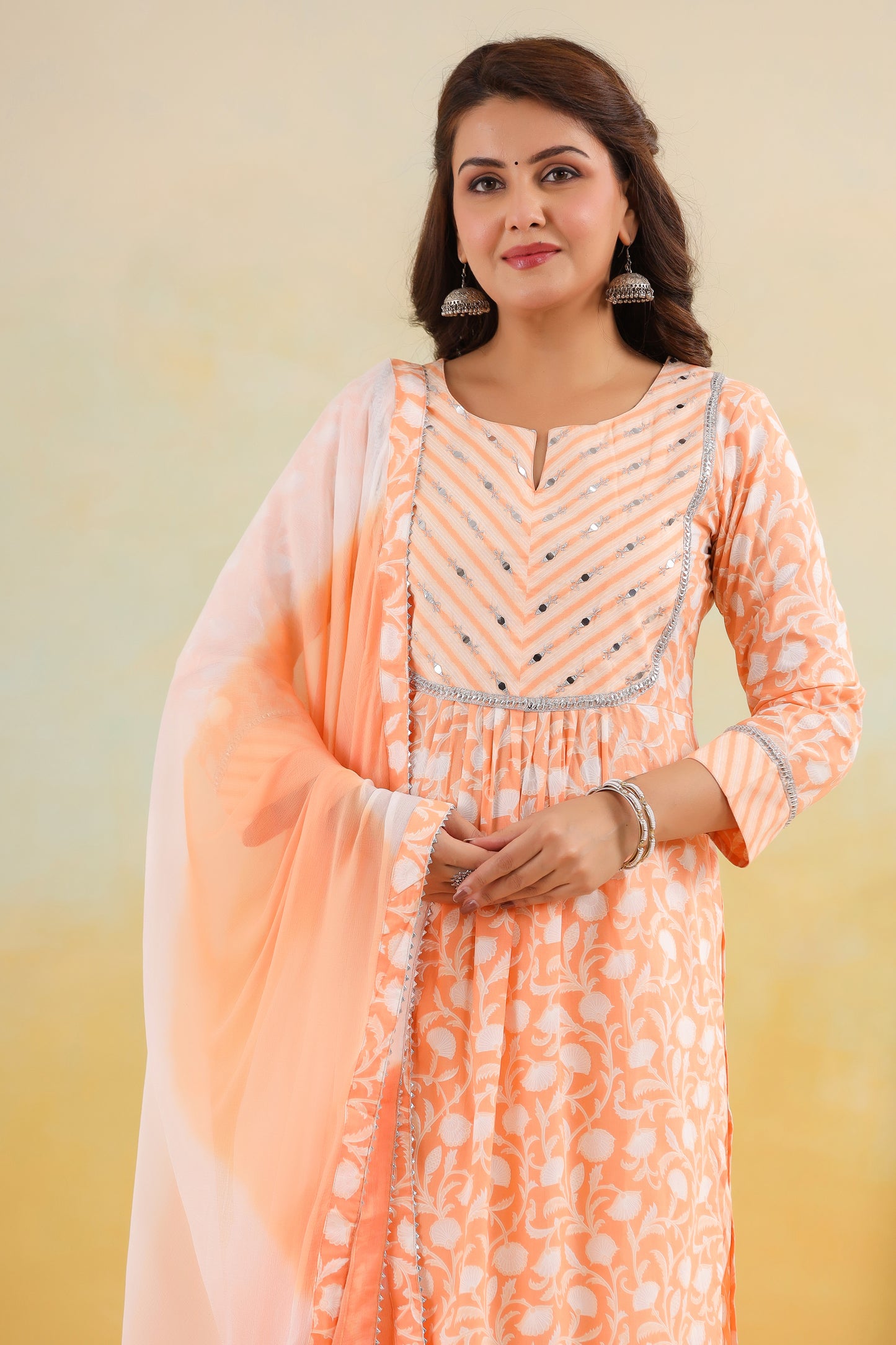 Woman wearing an orange and white traditional outfit with a light pink dupatta against a beige background