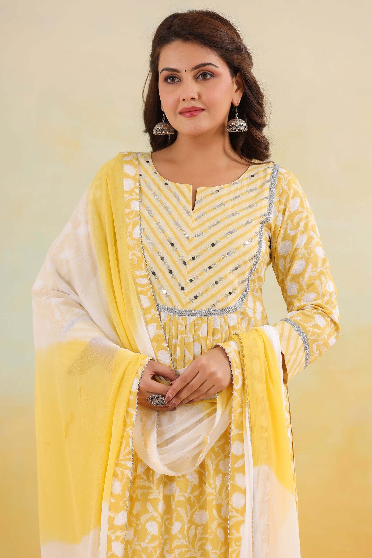 Woman wearing a yellow and white traditional outfit with a matching dupatta against a light background