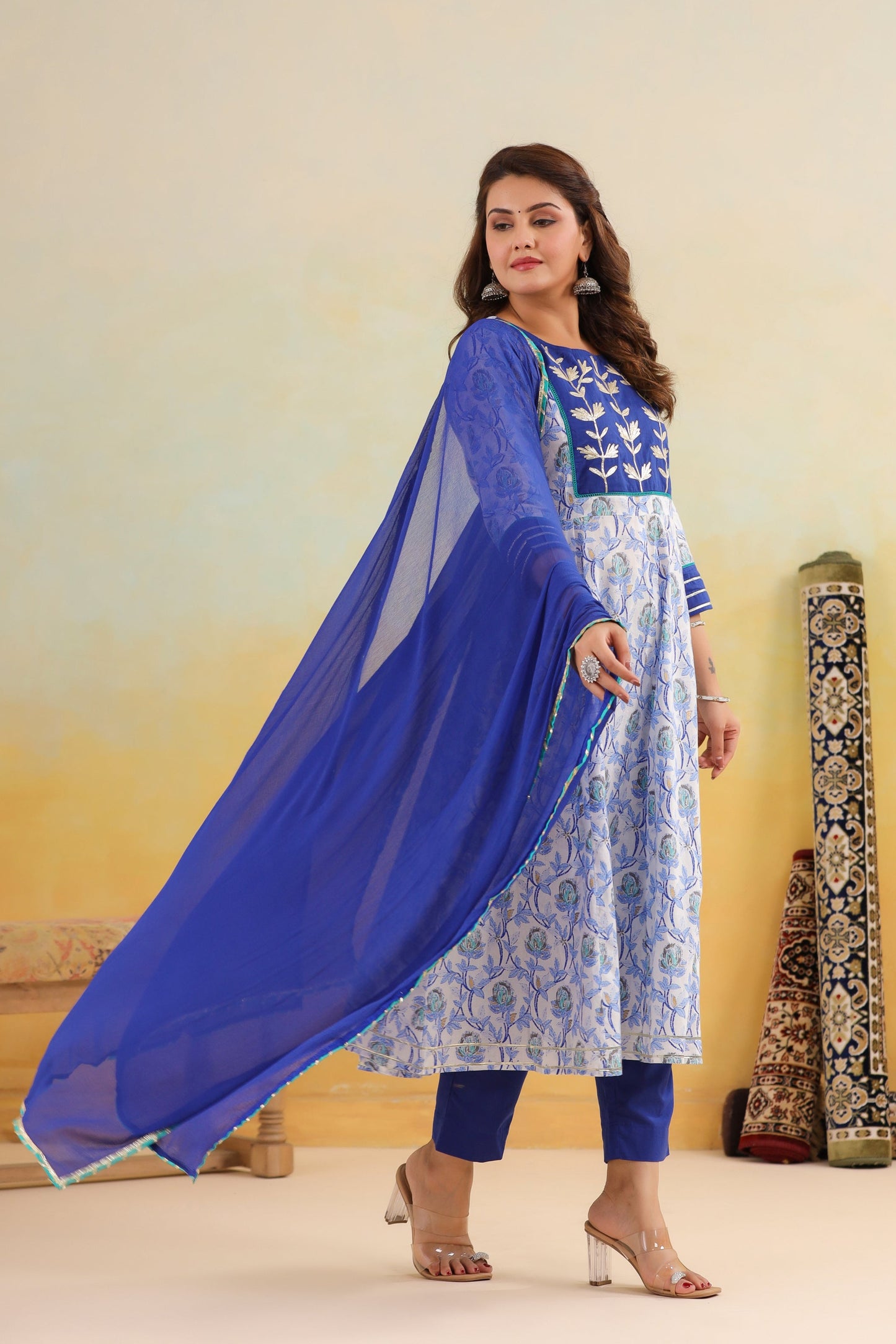 Woman wearing a blue and white traditional outfit with a sheer blue dupatta against a yellow background.