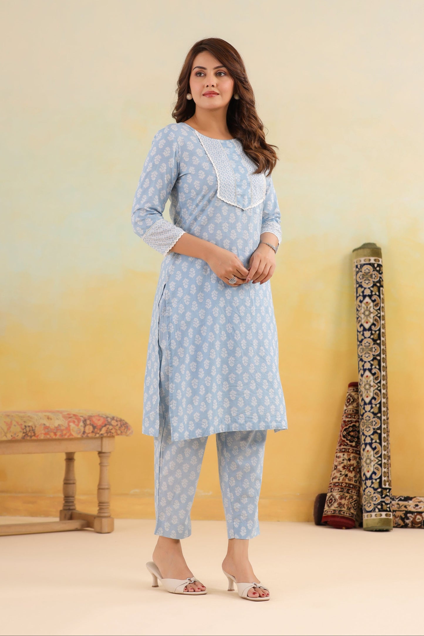 Woman wearing a light blue kurta with white patterns in a room with a yellow gradient wall.
