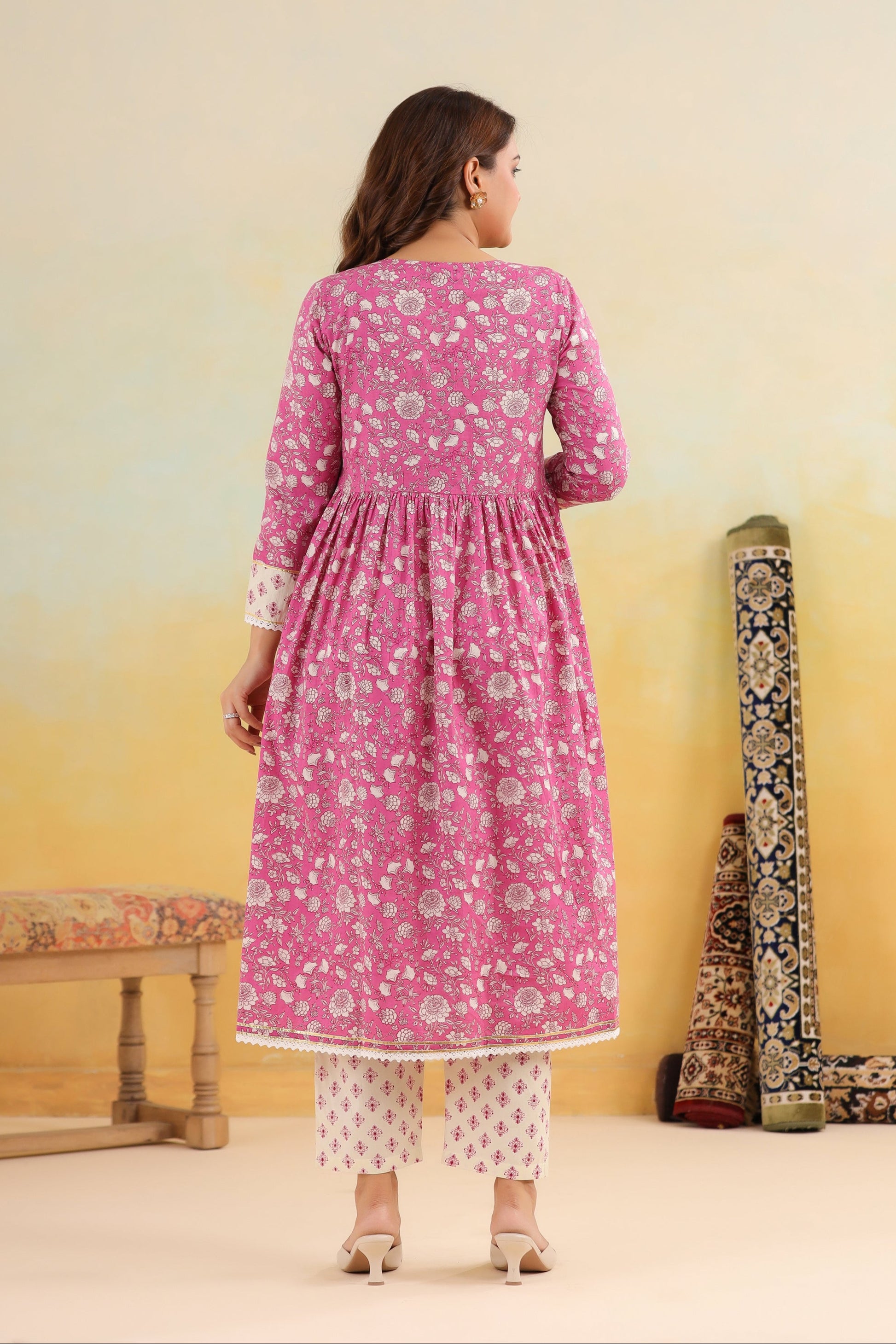 Woman wearing a pink floral dress with a yellow gradient wall and traditional instruments.