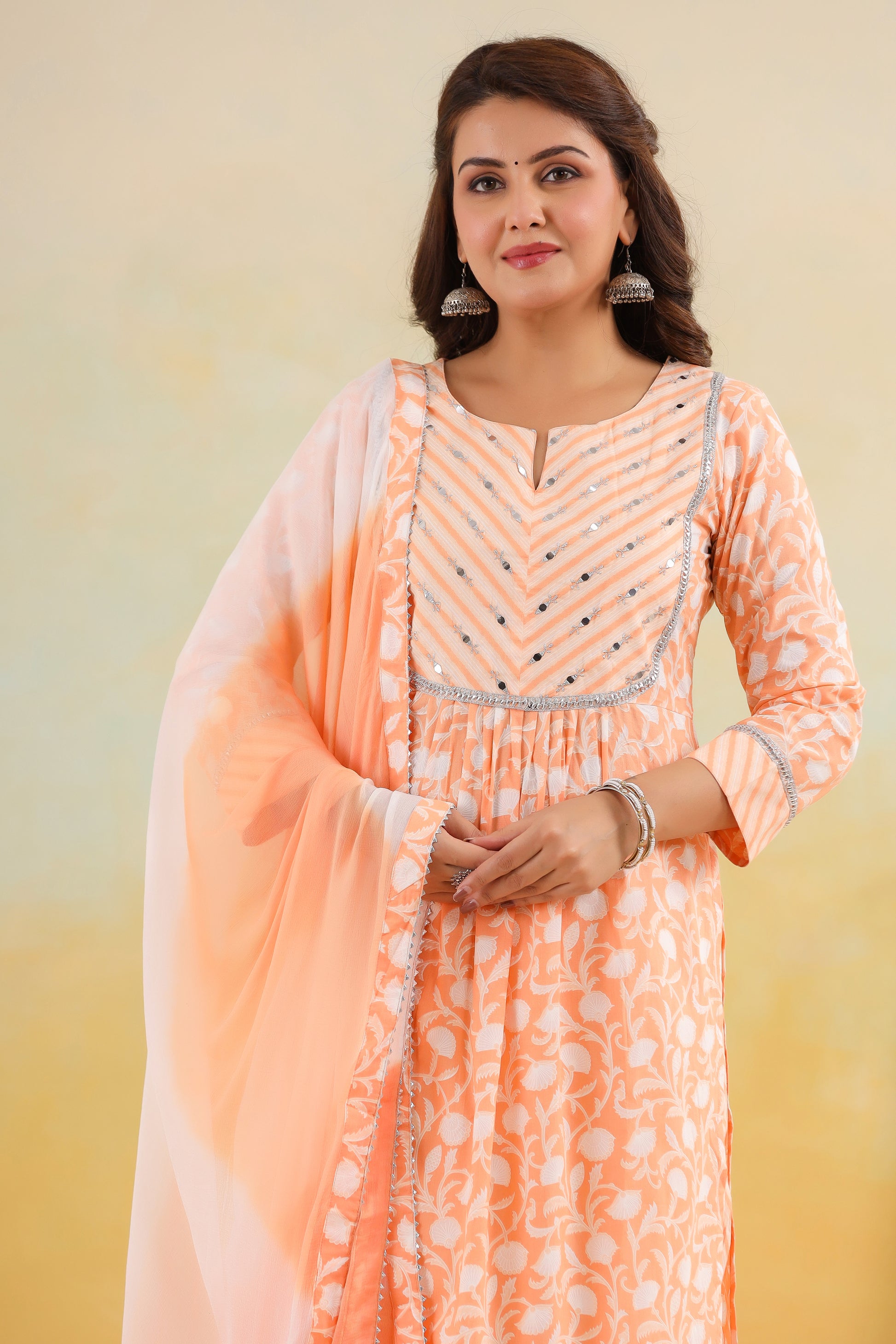 Woman wearing an orange and white traditional outfit with a light pink dupatta against a beige background