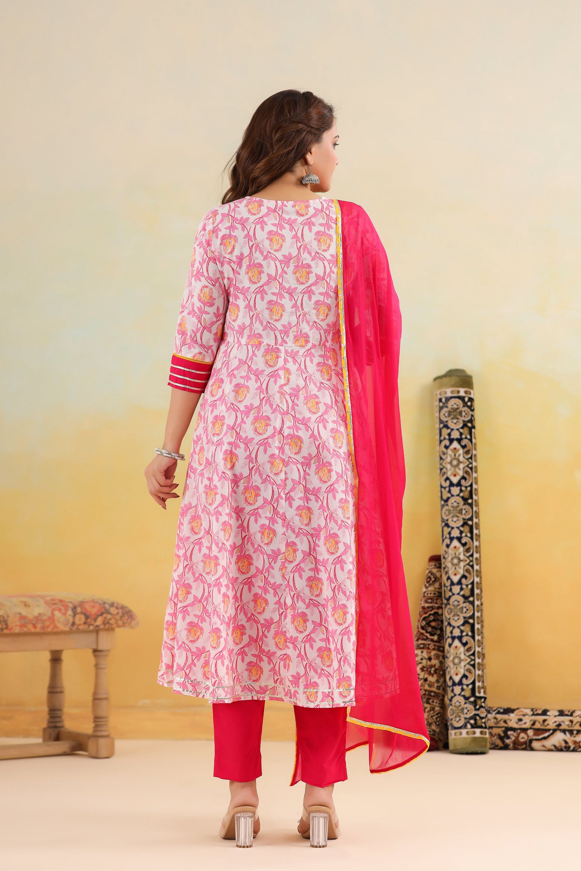Woman wearing a pink floral kurta with a matching dupatta in a minimal setting.