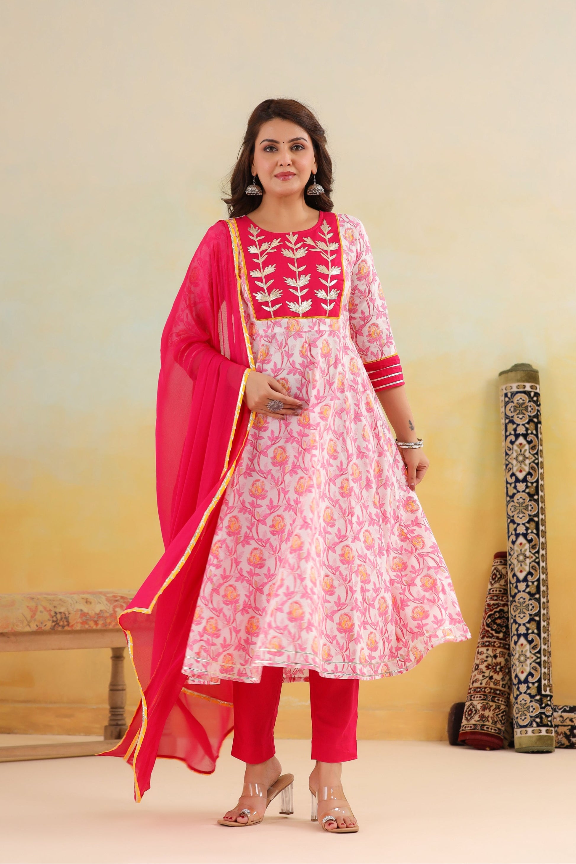 Woman in a pink and white traditional outfit with a dupatta, standing against a yellow background.