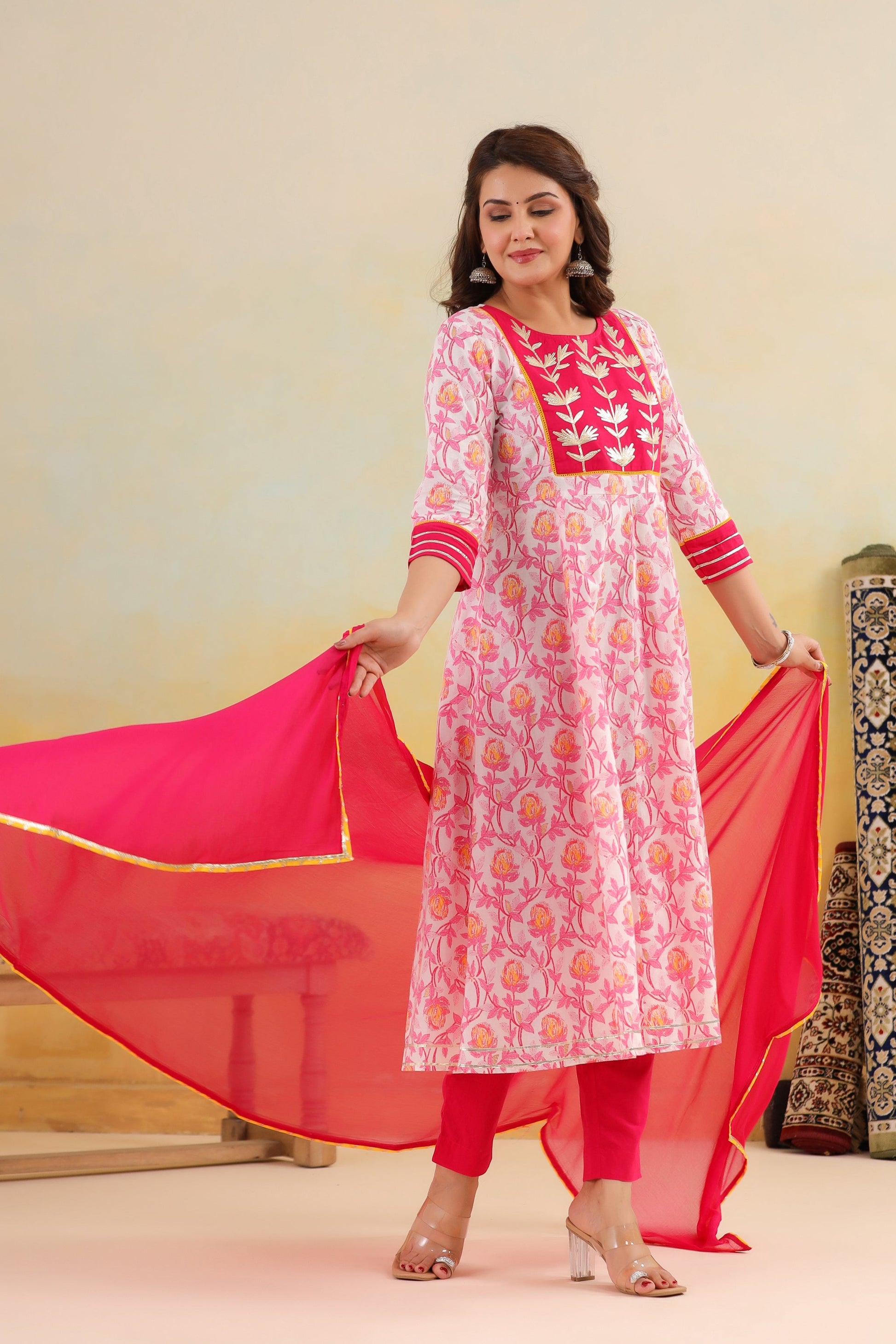 Woman wearing a pink and white traditional outfit with a red dupatta against a plain background