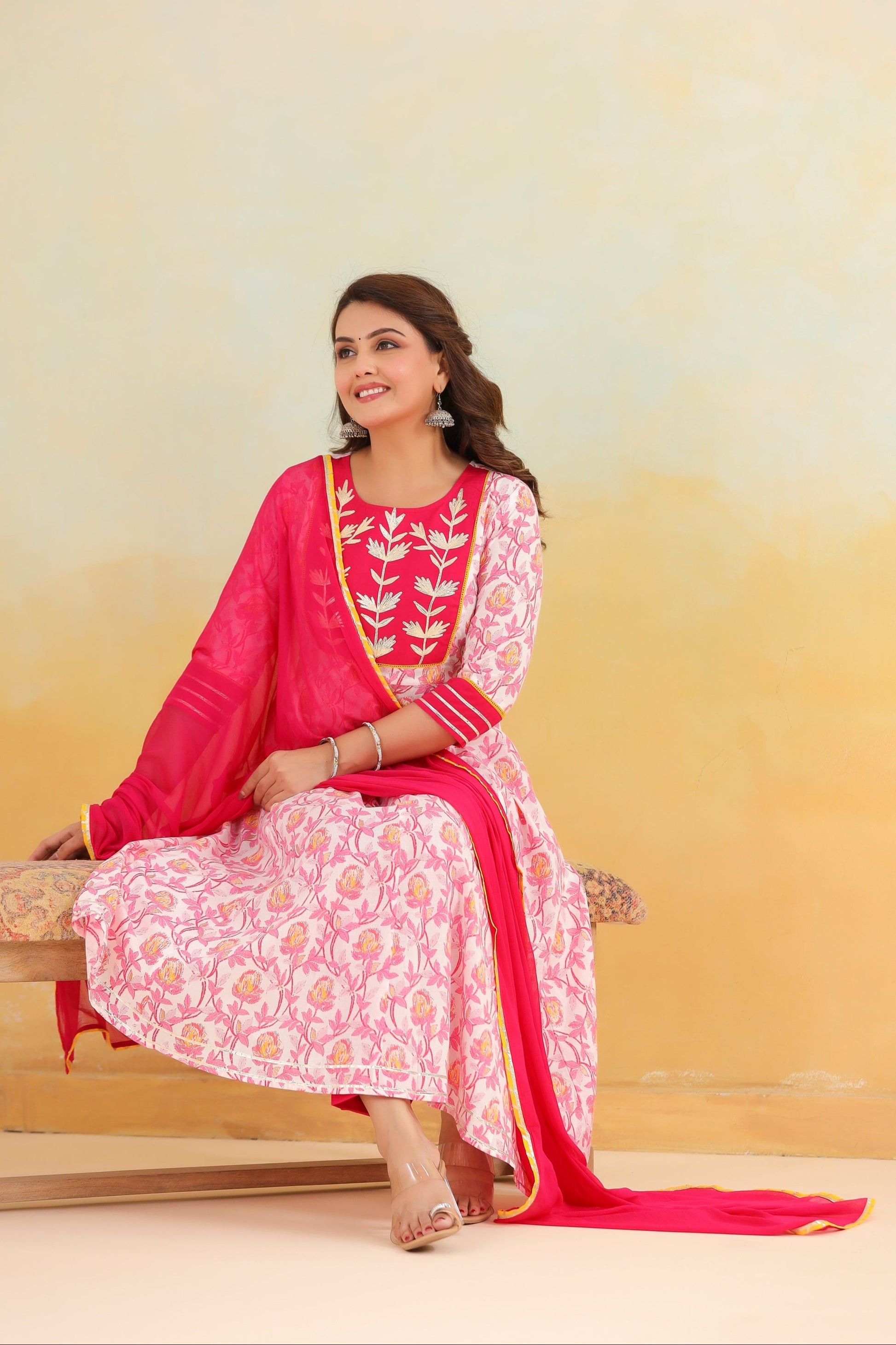 Woman in a pink and white traditional outfit sitting on a bench with a gradient yellow background