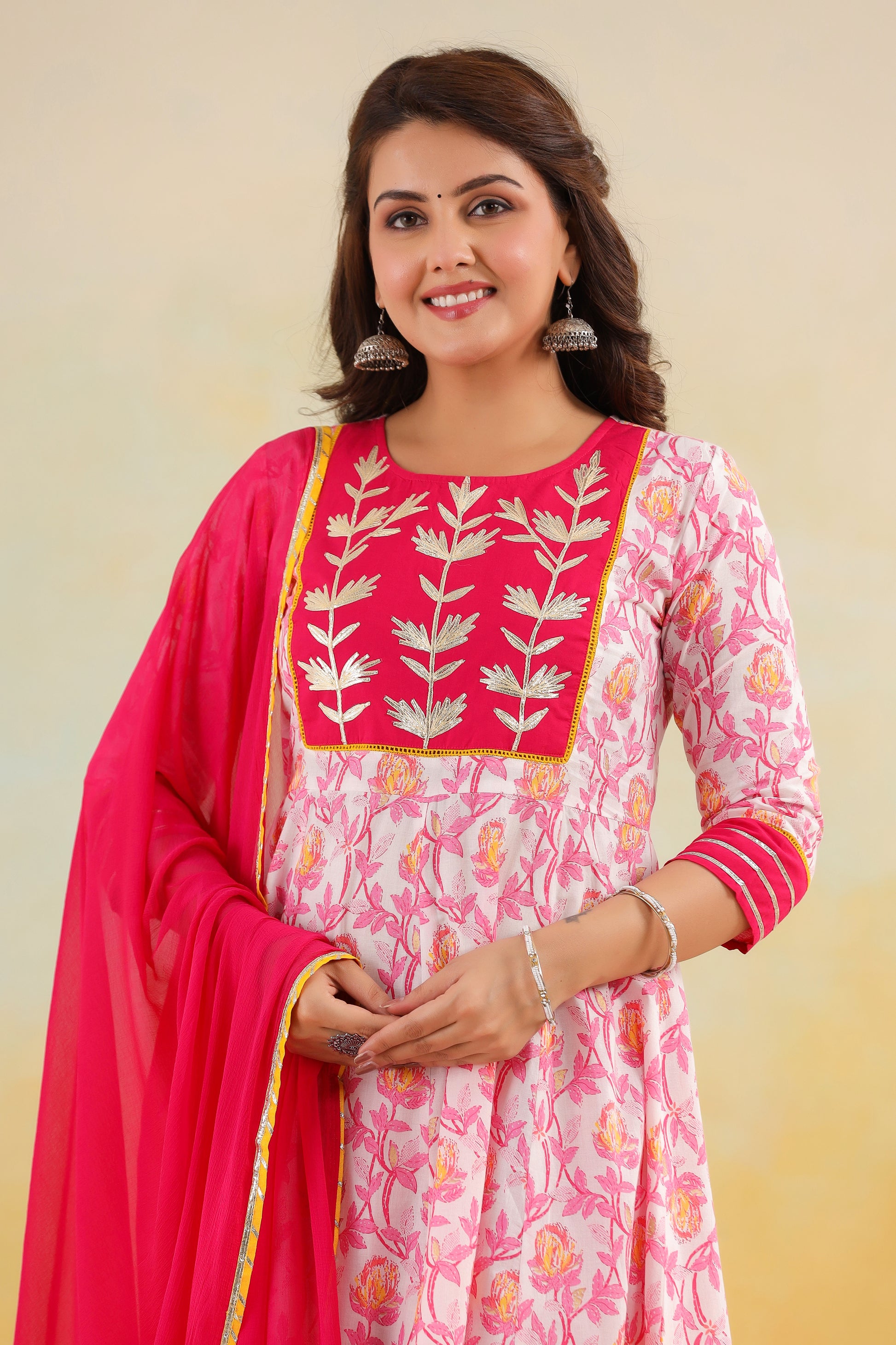 Woman wearing a pink and white embroidered dress with a red dupatta against a beige background