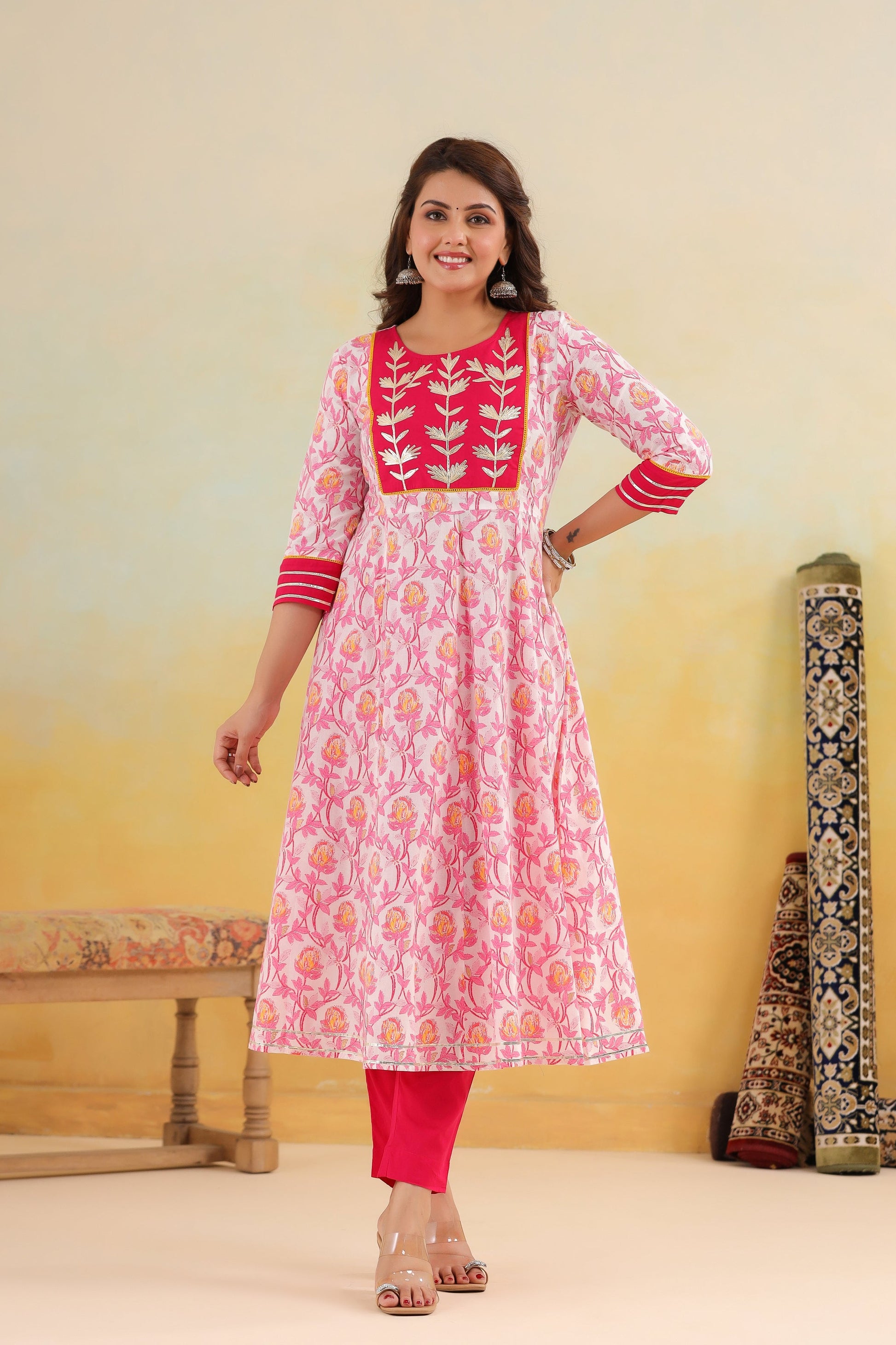 Woman wearing a pink and red traditional outfit with floral patterns against a yellow background