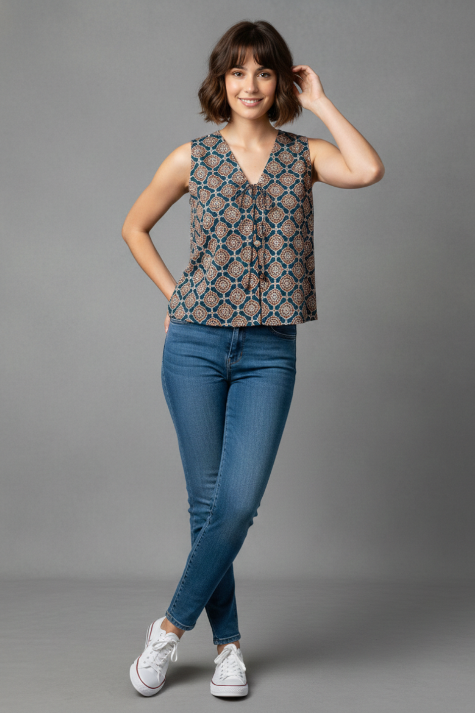 Woman wearing printed sleeveless top with V-neck and tie detail, paired with blue jeans and white sneakers