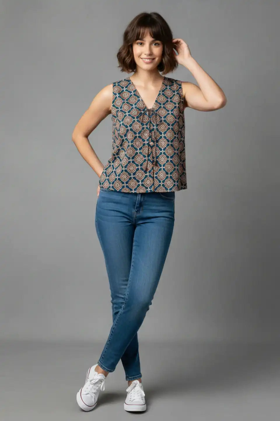 Woman wearing printed sleeveless top with V-neck and tie detail, paired with blue jeans and white sneakers
