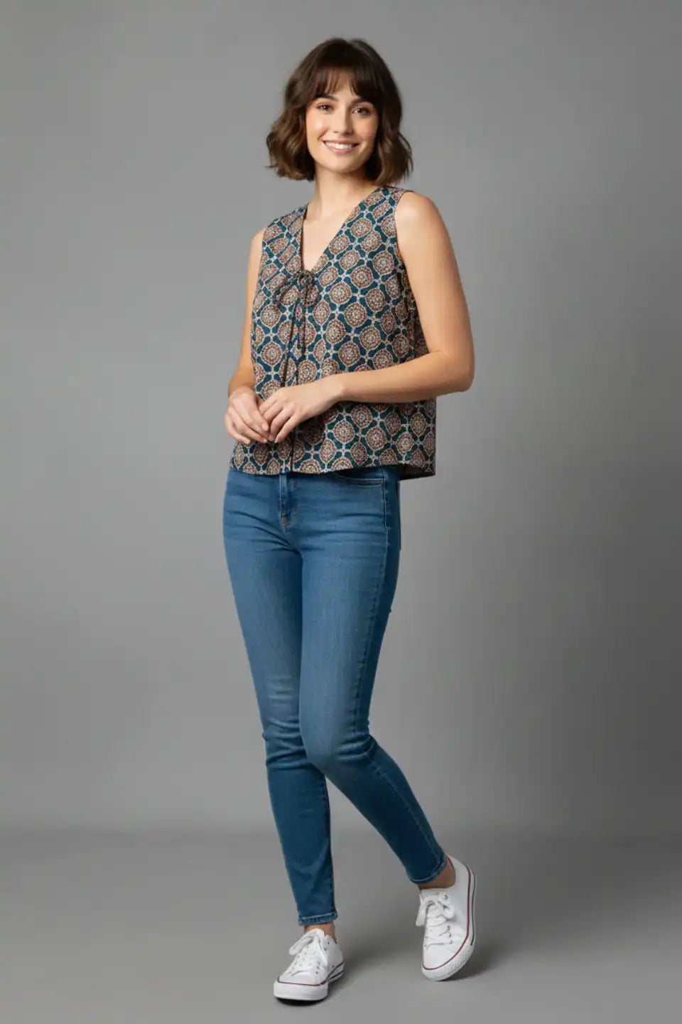 Woman wearing sleeveless patterned top with jeans and white sneakers, casual daily wear outfit